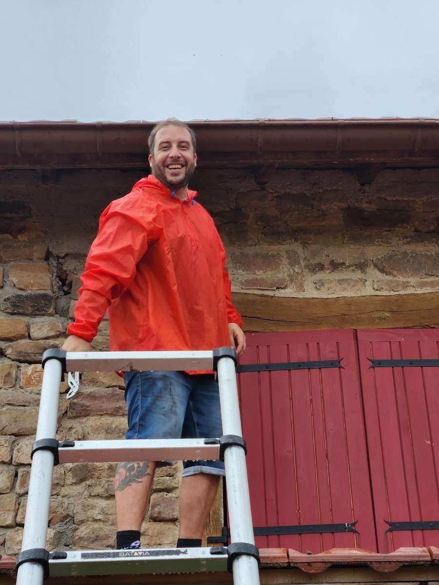 Roland, artisan couvreur de Roland Toiture, sur son échelle devant une toiture